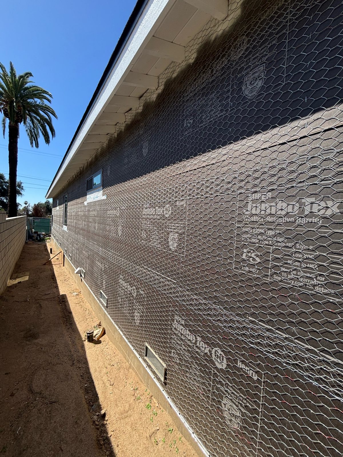 House wall in progress with weather-resistant paper and wire mesh installed before stucco