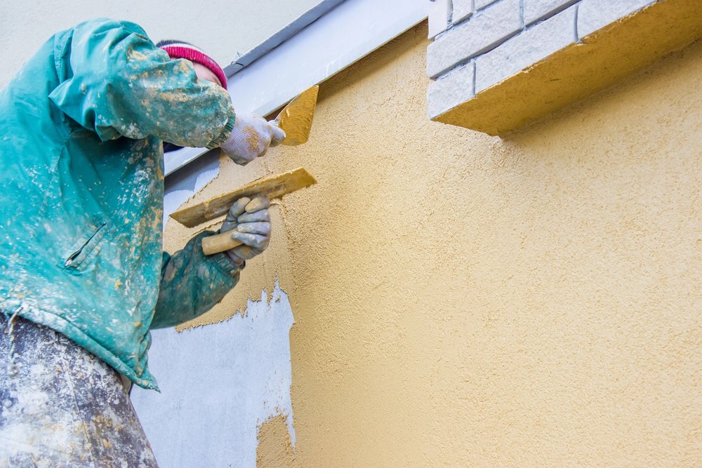 A worker troweling a fresh yellow color coat onto a stucco wall